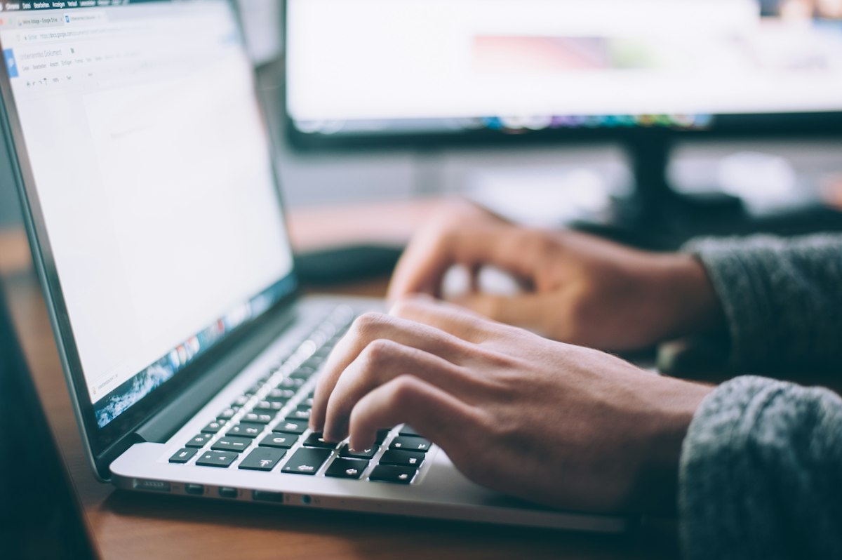 Hands typing on a laptop at a warm wood desk